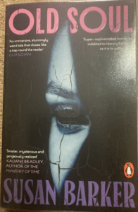 Cover of 'Old Soul' by susan Barker, showing an image of a sliver of a face - a single eye - peering out from a lack background. The face has the eyebrows and eyelashes of a human, but the empty eye socket of a doll, and the cracked surface of a statue. Copy of this book gratefully borrowed from Waltham Forest Libraries.